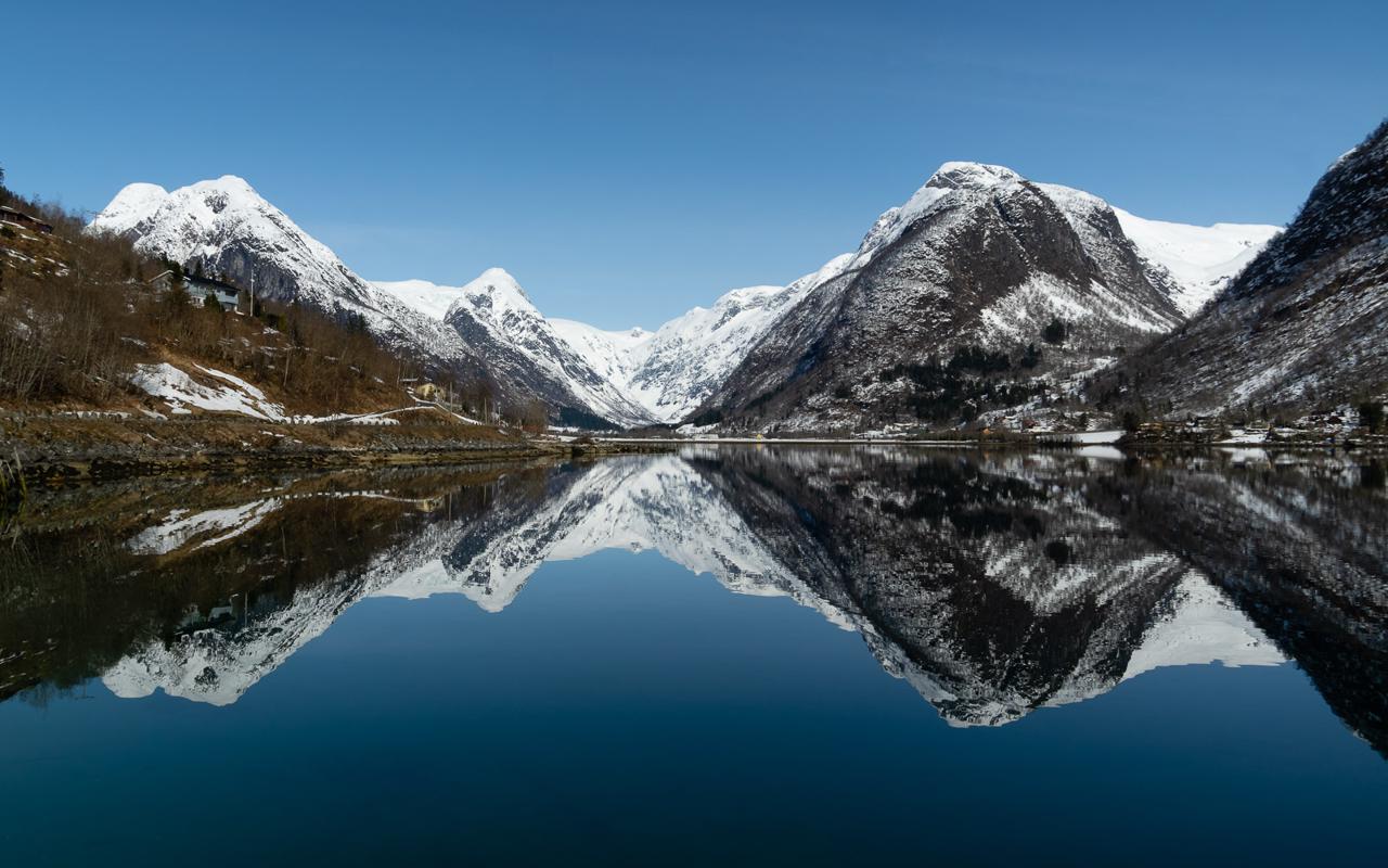 Snow-capped mountains mirrored in a still fjord at Fjærland, Norway.